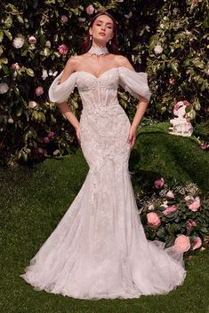 a woman in a white wedding dress standing on the grass with flowers behind her,