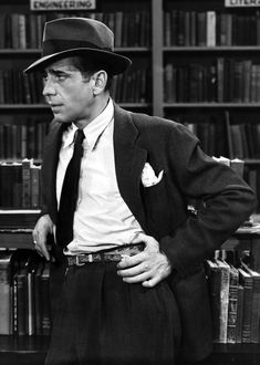 a man in a suit and hat standing next to bookshelves