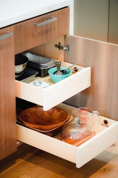 an open drawer in a kitchen with bowls and plates on the bottom shelf next to it