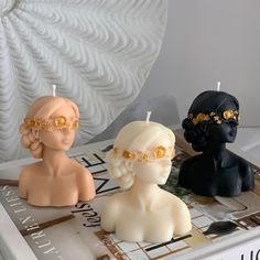 three candles are sitting on top of a book with decorative head pieces in front of them