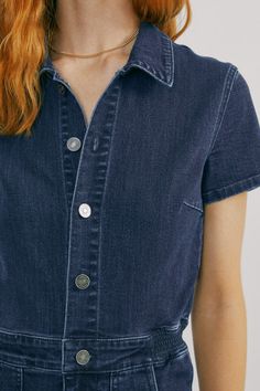 Our "Denim Utility Jumpsuit" is a dark washed denim jumpsuit. It buttons down the front and has front pockets. Our model is wearing a size Large. Casual Overalls With Button Closure, Casual Short Sleeve Overalls With Button Closure, Casual Denim Blue Jumpsuit With Buttons, Casual Overalls With Button Closure And Short Sleeves, Casual Short Sleeve Denim Jumpsuit With Buttons, Medium Wash Short Sleeve Jumpsuit With Button Closure, Medium Wash Denim Jumpsuit With Short Sleeves And Buttons, Cotton Denim Button-up Jumpsuit, Button-up Cotton Denim Jumpsuit