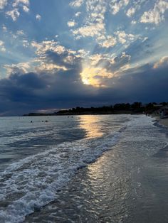 the sun is setting over the ocean with waves coming in to shore and people swimming in the water