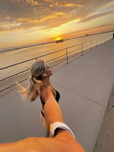 a woman is pointing her finger at the sun setting over the ocean with another person in the background