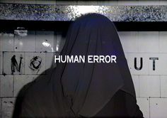 a woman in a black hoodie standing next to a wall with the words human error written on it