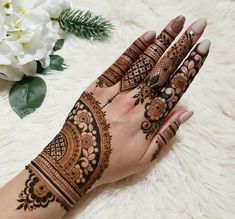 a woman's hand with henna tattoos on it and flowers in the background