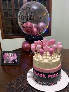 a birthday cake with pink and black decorations on it, sitting on a table in front of balloons