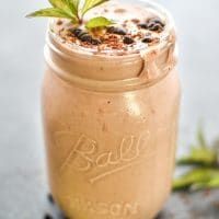 a close up of a drink in a mason jar with a plant growing out of it