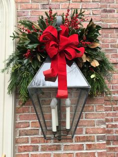 a christmas wreath on the side of a brick building with a red bow and two white candles