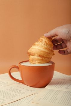 a person is holding a pastry in a cup on top of some books and papers