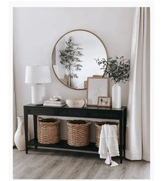 a black console table with two baskets and a round mirror on it's wall