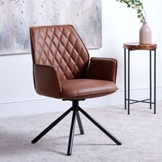 a brown leather office chair sitting in front of a table with a vase on it