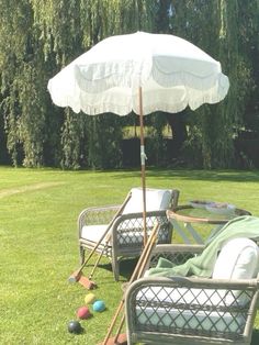 two lawn chairs and an umbrella in the middle of a yard with balls on the grass