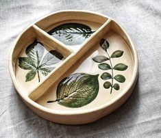 a wooden bowl with leaves painted on the side and two spoons in front of it