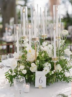 a table with candles and white flowers on it, along with place cards for the number six