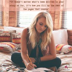 a woman sitting on top of a bed holding a pen and writing in a book