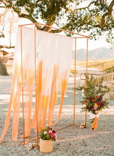 an outdoor ceremony setup with orange drapes and flowers on the ground next to it