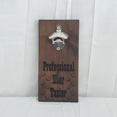 a wooden sign that says professional beer taster with a bottle opener hanging from it's side