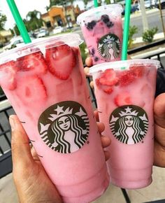 three starbucks drinks with strawberries and blueberries in them are being held by two people