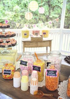 a table topped with jars filled with candy and cupcakes next to other items