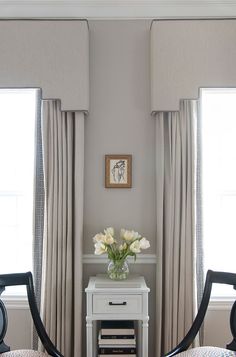 two chairs and a table with flowers on it in front of the window, one is white