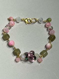 Gorgeous glass beads make up this bracelet and give it a cohesive yet unique feel as the pink and green colors reflect the design inside the butterfly and white beads. Those beads feature pink flowers with green leaves inlaid with the white having gold streaks as well. Beautifully soft bracelet gives the feel of a forest fairy or a perfect accessory for a tea party.  Durable beads and connections make this bracelet perfect for everyday  or heavy use. May break under extreme unintended use.  Made to fit. For Reference, the bracelet in the photo is 7.5 inches long and is standard size, smaller wrist chose 7 inches to ensure snug fit. Male standard size is 8 inches.  Larger sizes will have bead pattern repeated until desired length.  Each item bought will be set with an assortment of freebies Pink Glass Jewelry With Colorful Beads, Pink Glass Jewelry With Faceted Beads, Pink Glass Beaded Bracelets As Gift, Handmade Pink Glass Bracelets, Adjustable Pink Glass Bracelets, Adjustable Pink Bracelets, Pink Flower Glass Jewelry, Pink Flower-shaped Glass Jewelry, Pink Beaded Glass Bracelets