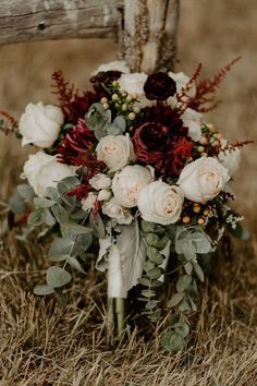 a bridal bouquet with red and white flowers sits on the ground next to a wooden fence