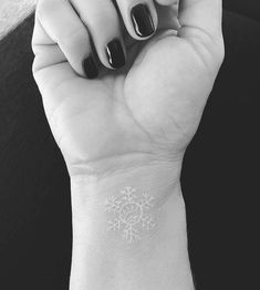 a woman's wrist with a snowflake tattoo on her left hand and a black - and - white background