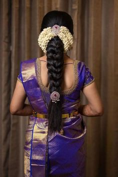 a woman in a purple sari with braids and flowers on her head is looking back