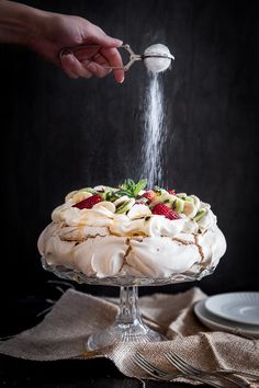 someone sprinkling icing on a cake with fruit