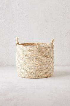 a white basket with rope handles on the top and bottom, sitting against a wall