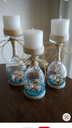 three glass vases filled with sand and sea shells on top of a wooden table