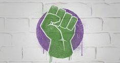 a fist painted on a brick wall with purple and green splatters around it