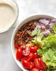 a white bowl filled with salad and dressing next to a glass of ranch dressing on a marble surface