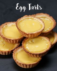 four small tarts sitting on top of a black surface with the words egg tarts above them