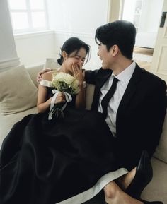 a man and woman sitting on top of a couch next to each other holding flowers