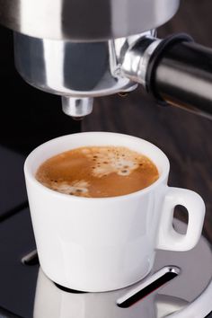 a cup of coffee sitting on top of a saucer next to a metal faucet