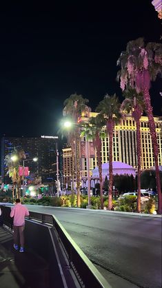 a woman walking down the street at night with palm trees and buildings in the background