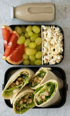 an open lunch box with grapes, grapefruit, and burritos