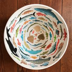 a bowl with fish painted on it sitting on a wooden floor next to a wall