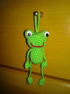 a crocheted frog keychain hanging from a wooden door with eyes wide open