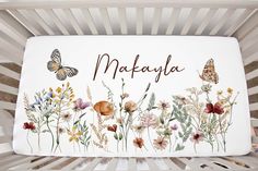 a white crib with flowers and butterflies painted on the side that says makayla