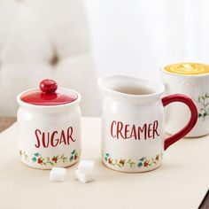 two white mugs with red lids sitting on top of a table next to marshmallows