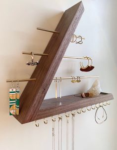 a triangle shaped shelf with jewelry hanging from it's sides and two pairs of earrings on hooks