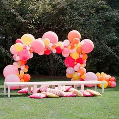 a bunch of balloons that are on a bench in the grass with some trees behind it