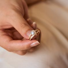 a woman's hand holding a pearl and diamond ring