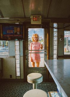 a woman in pink dress standing at the entrance to a diner with two stools