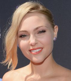 a woman with blonde hair and blue eyes smiles at the camera while wearing an orange dress