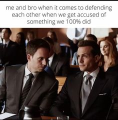 two men in suits sitting next to each other at a table with people behind them