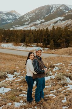 a man and woman standing in the middle of a field with mountains in the background