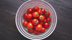 a white basket filled with lots of red tomatoes on top of a wooden table next to a knife and fork